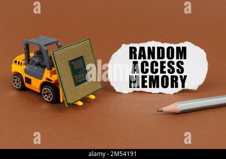 Technological concept. On a brown surface, a forklift is transporting a processor, next to it is paper with the inscription - Random Access Memory Stock Photo