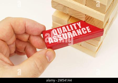 Business and technology concept. From the tower with wooden planks, they take out a red plaque with the inscription - Quality Assurance Stock Photo