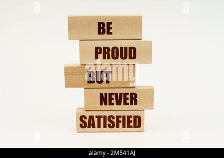 Business concept. On a white surface are wooden blocks with the inscription - BE PROUD BUT NEVER SATISFIED Stock Photo