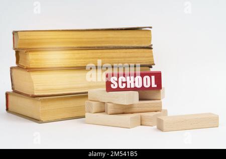 Education concept. On a white surface, a stack of books and wooden blocks, on a red block there is an inscription - school Stock Photo