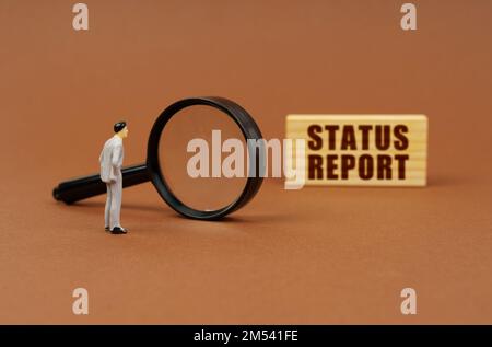 Business concept. A figurine of a businesswoman looks through a magnifying glass at a block with the inscription - STATUS REPORT. Block blurred Stock Photo