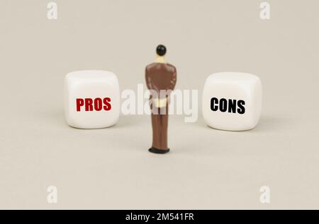 Business concept. A human figurine stands in front of white cubes with inscriptions - Pros and cons Stock Photo