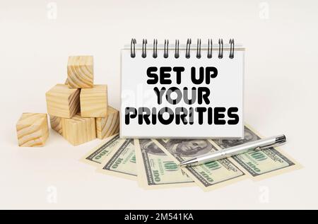 Business concept. On a white surface, cubes, dollars, a pen and a notepad with the inscription - SET UP YOUR PRIORITIES Stock Photo