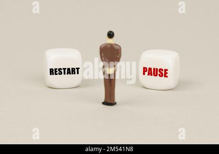 Business concept. A human figurine stands in front of white cubes with inscriptions - restart and pause Stock Photo