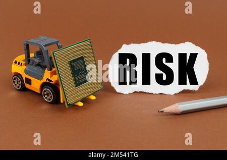 Technological concept. On a brown surface, a forklift is transporting a processor, next to it is paper with the inscription - RISK Stock Photo