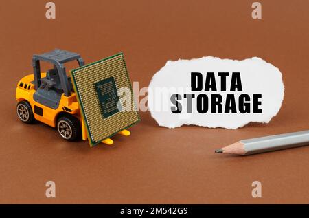 Technological concept. On a brown surface, a forklift is transporting a processor, next to it is paper with the inscription - Data Storage Stock Photo