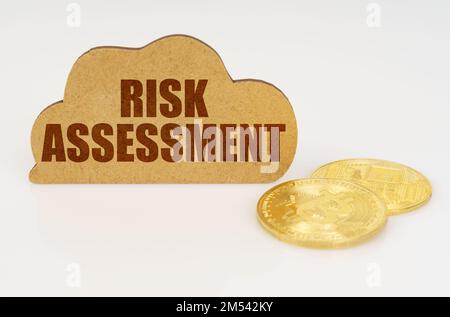 Business and technology concept. Bitcoins lie on a white surface and there is a sign - a cloud with the inscription - RISK ASSESSMENT Stock Photo