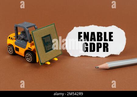 Technological concept. On a brown surface, a forklift is transporting a processor, next to it is paper with the inscription - enable GDPR Stock Photo