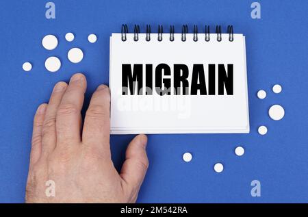 Medical concept. On the blue surface of the tablet, a hand and a notepad with the inscription - MIGRAIN Stock Photo