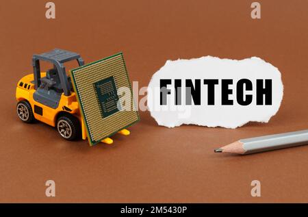 Technological concept. On a brown surface, a forklift is transporting a processor, next to it is paper with the inscription - fintech Stock Photo