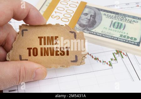 Business and finance concept. Against the background of dollars and a chart of quotations, a man holds a sign in his hands with the inscription - TIME Stock Photo