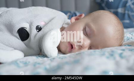 infancy, childhood, development, medicine and health concept - close-up face of sweaty newborn chubby sleeping baby 10 month with pacifier lying on Stock Photo