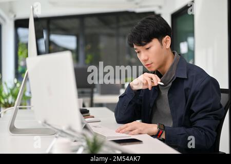 Handsome and smart young Asian male programmer working at his office desk. Young male officer working on his task. Stock Photo