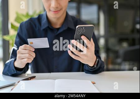 Close up view of young man doing online shopping while holding smartphone and credit card. online shopping, transferring money, cashless payment Stock Photo