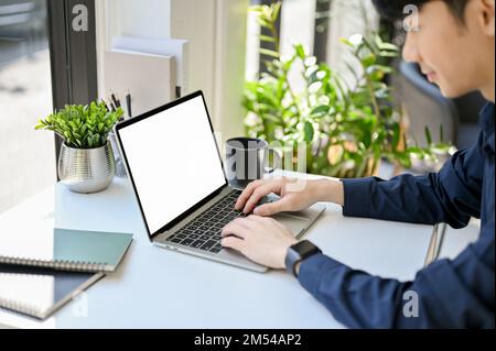 Handsome and focused young Asian male employee working on his task on laptop computer. close-up, side view image, laptop white screen mockup Stock Photo