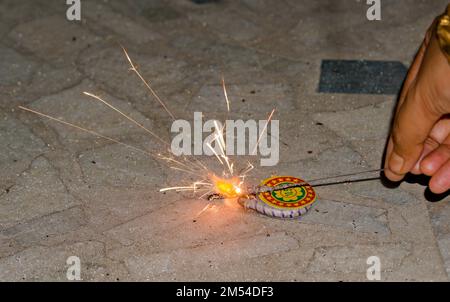 igniting ground spinner with the help of sparkler during diwali. Stock Photo