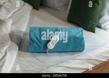 Folded electric heating pad with controller on bed at night, closeup Stock Photo