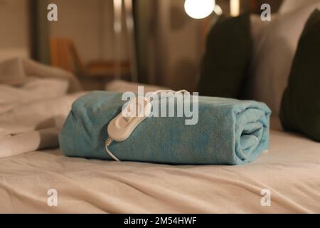 Folded electric heating pad with controller on bed at night, closeup Stock Photo