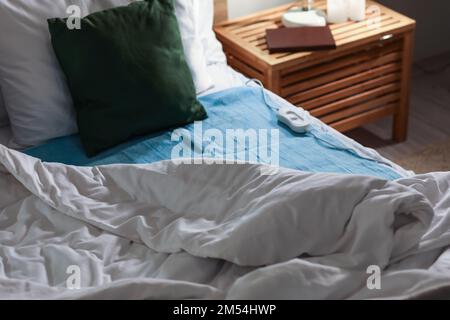 Bed with electric heating pad in bedroom at night Stock Photo