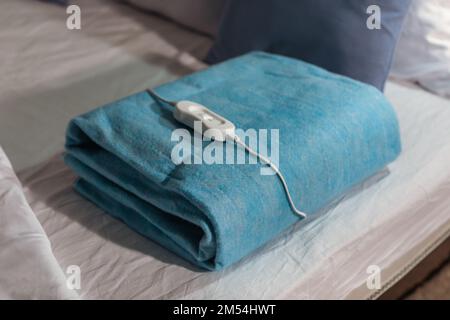 Folded electric heating pad with controller on bed at night, closeup Stock Photo