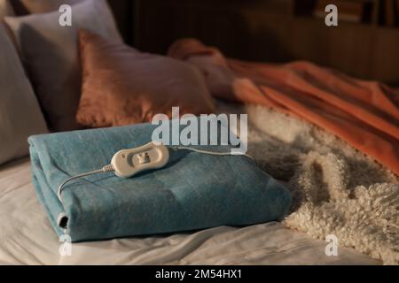 Folded electric heating pad with controller on bed at night, closeup Stock Photo