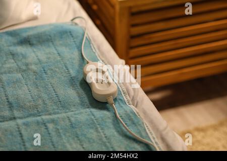 Electric heating pad with controller on bed at night, closeup Stock Photo