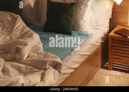 Bed with electric heating pad in bedroom at night Stock Photo