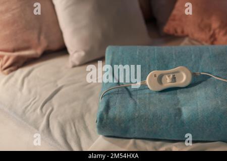 Folded electric heating pad with controller on bed at night, closeup Stock Photo