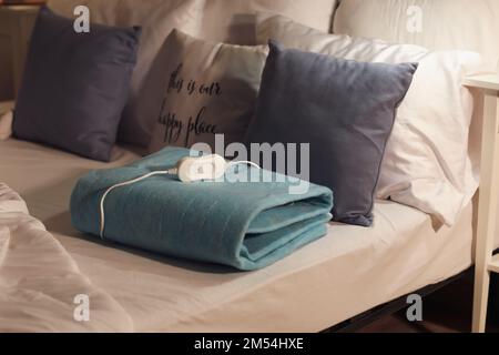 Folded electric heating pad with controller on bed at night, closeup Stock Photo
