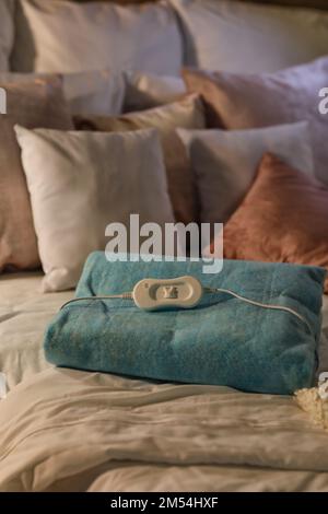 Folded electric heating pad with controller on bed at night, closeup Stock Photo