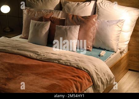 Bed with electric heating pad in bedroom at night Stock Photo