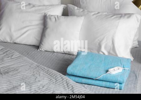 Folded electric heating pad with controller on bed in bedroom Stock Photo