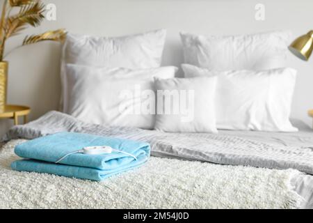 Folded electric heating pad with controller on bed in bedroom Stock Photo