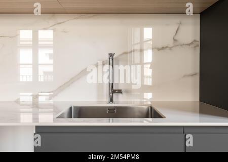 Modern small square sink in the kitchen. Fashionable built-in stainless steel sink. Interior kitchen in white and gray colors with marble tiles on the Stock Photo