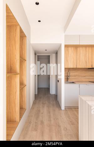Long passage through kitchen with hardwood floors to another part of house with door on opposite side. Kitchen with light wood furniture. There is Stock Photo