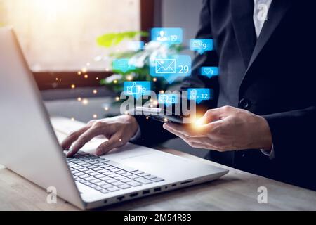 Chat and blue notification on smartphone, notebook (Laptop) with emoji social media icon. Businessman using smartphone on vacation with hologram. Soci Stock Photo