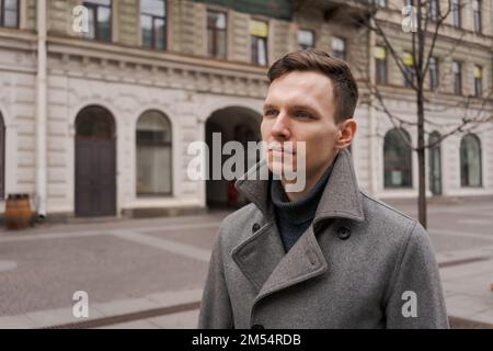 Young man walking down street, autumn or winter cold day. Outdoors, outside. Gorgeous guy in gray coat in city street Stock Photo