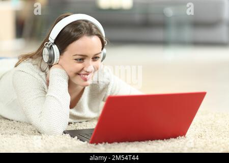 Happy teen wearing headphones watching media on laptop on the floor at home Stock Photo