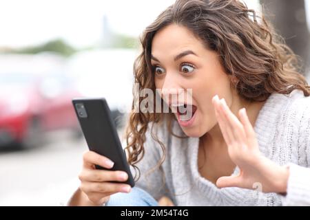 Surprised woman checking smart phone content in the street Stock Photo