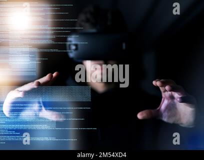 Technology made tangible. a young computer programmer wearing a vr headset while working on his code. Stock Photo