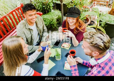 From above of positive multiracial friends drinking coffee and looking at each other while having breakfast on terrace of cafe Stock Photo