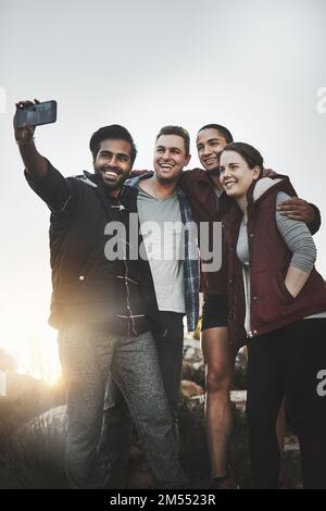 Taking selfies over a breathtaking view. a group of friends taking selfies while hiking together in the mountains. Stock Photo