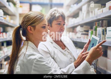 We are the front-line of healthcare. two pharmacists using a digital tablet while checking stock on the shelf. Stock Photo