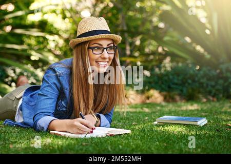 Jotting in her journal. an attractive young woman writing in her diary while outside on the grass. Stock Photo