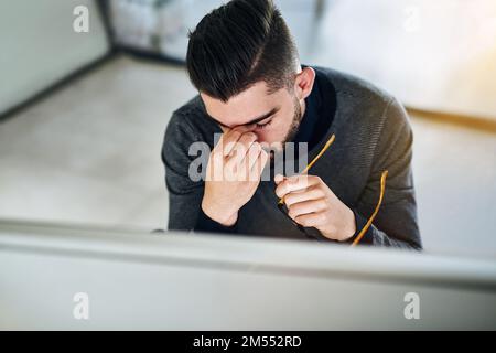 All this tension is bringing on a headache. a young designer looking stressed out while working in an office. Stock Photo