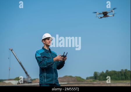 A man in a helmet and overalls controls a drone at a construction site. The builder carries out technical oversight. Stock Photo