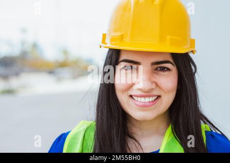 young latin woman engineer, wearing safety helmet and vest, worker of a construction site, standing on the street smiling looking at the camera, copy Stock Photo