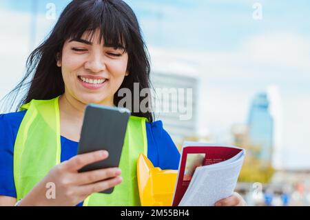 closeup of latin young female engineer on her lunch break, smiling checking phone, smiling looking at mobile screen. Stock Photo