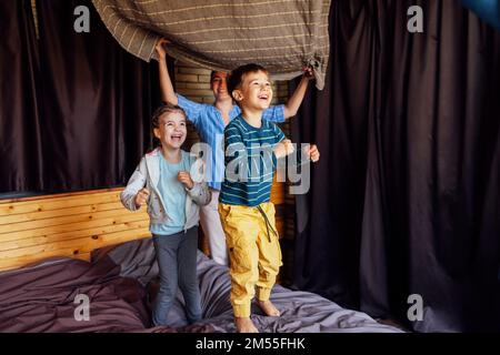 Happy family multiethnic mother, father and kids, son and daughter, laughing, playing, fights pillows and jumping in bed in bedroom at home in the mor Stock Photo