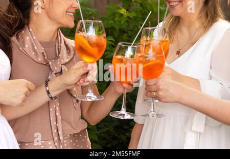 Happy friends spending time together, focus on young women drinking Aperol spritz cocktail. Summer wedding party. Happiness and celebration concept Stock Photo